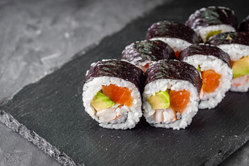 appetizing sushi roll futomaki salmon, shrimp and avocado on a black stone plate
