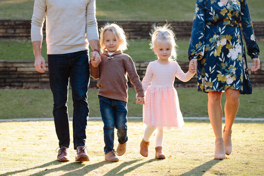 Two young children walking and holding hands with their parents