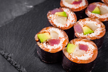 appetizing sushi roll with tuna salmon escolar crab and avocado on a black stone plate