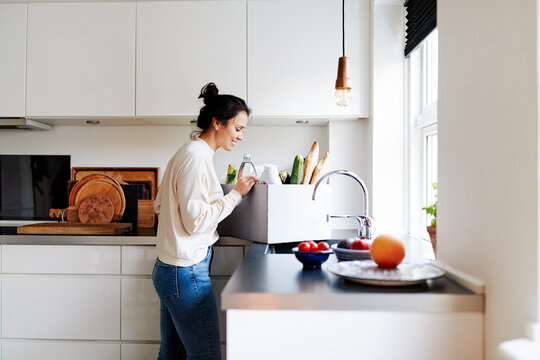 Woman Unpacking Groceries At Her Kitchen Counter