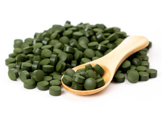 Spirulina algae tablets with a wooden spoon isolated on white background. Nutritional supplements, vitamins and health concept