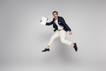 Fototapeta na wymiar full length of young businessman holding paper folder while flying on grey
