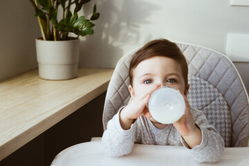 Lovely baby boy age of 1 year drinking milk from a small bottle, kids breakfast food