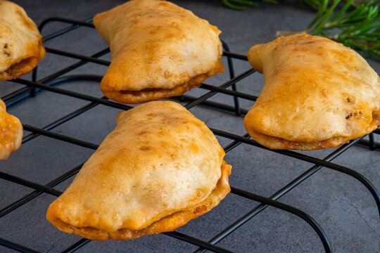Homemade freshly baked empanadas pastry with meat filling. Gluten-free version of an authentic traditional Spanish Latin America cuisine food on a black cooling rack and gray background. Close up.