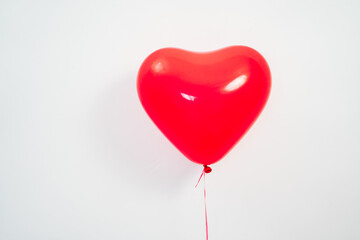 A heart shaped red balloon in hand against a white wall. 