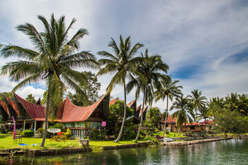 Batak houses with red roof with palm trees around at the lake Toba in Sumatra, Indonesia, 