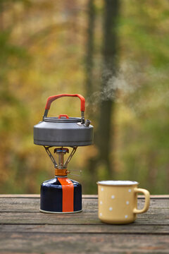 A kettle boiling in the open air with a metal cup.