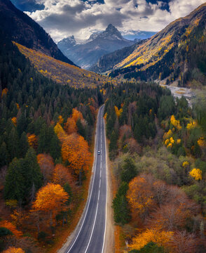 The road through the autumn forest towards the epic mountain