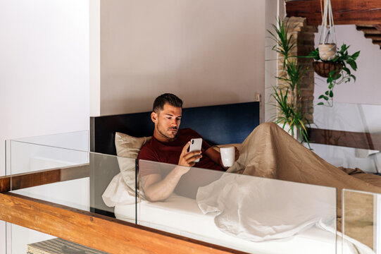 Man browsing smartphone in bed in morning