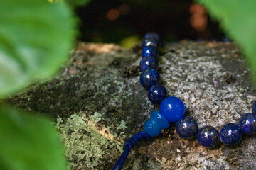 Close up of blue mala beads on stone between green leaves. Buddhist prayer beads for japa meditation