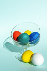 Hand-painted colorful Easter eggs in a transparent glass bowl on a light blue background, vertical frame, copy space