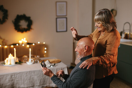 Cheerful senior couple communicating with friends via smartphone during Christmas holiday