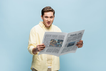 surprised young man in shirt reading travel newspaper isolated on blue