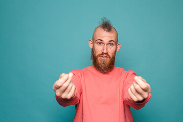 Bearded european man in casual peach isolated on turquoise background rubbing fingers doing money gesture