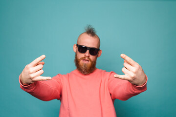 Fototapeta premium Bearded european man in casual peach isolated on turquoise background shouting with crazy expression doing rock symbol with hands up