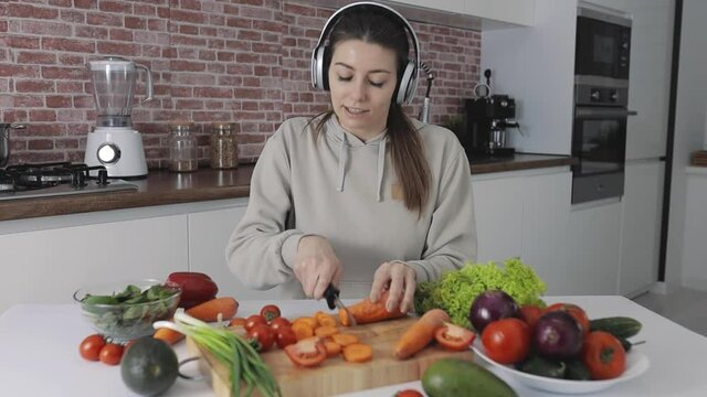 Young female preparing a vegan recipe, cutting vegetables and listening to music. Healthy lifestyle.