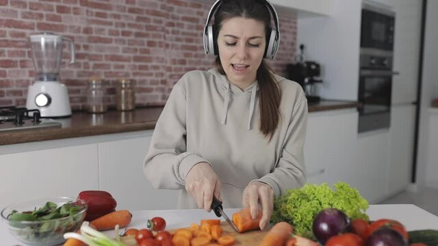 Healthy lifestyle. Young female preparing a vegan recipe, cutting vegetables and listening to music. Close-up.