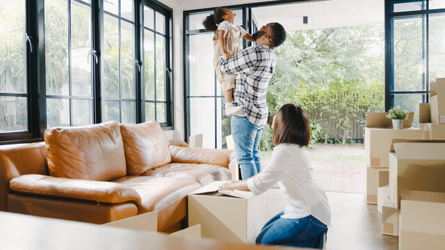 Happy African American young family bought new house. Mom, Dad, and child happy hold cardboard boxes for move object and having fun laugh into modern home. New real estate dwelling, loan and mortgage.
