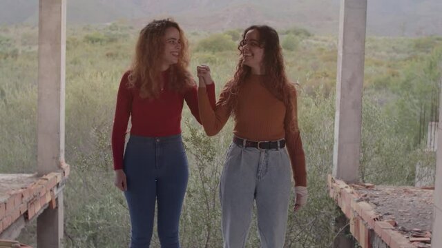 Hermanas gemelas agarradas de la mano mostrando amistad, felicidad y complicidad en un d&iacute;a nublado