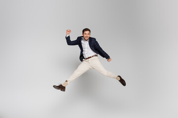 full length of happy young man with clenched fists levitating on grey