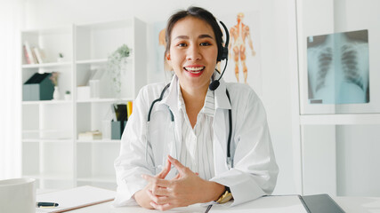 Young Asia lady doctor in white medical uniform with stethoscope using computer laptop talk video...