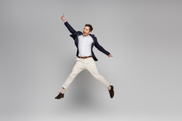 Fototapeta na wymiar full length of excited young man with outstretched hands levitating on grey