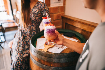 a group of friends sits on the terrace in the summer behind a wooden barrel with cocktails and a snack. without faces
