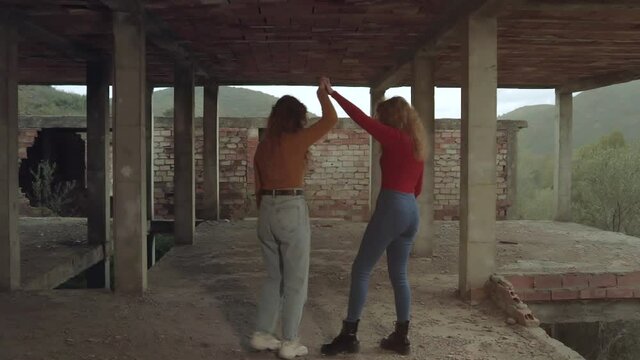 Hermanas gemelas jóvenes y pelirrojas bailando en una construcción al atardecer en un día nublado