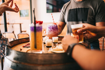 a group of friends sits on the terrace in the summer behind a wooden barrel with cocktails and a snack