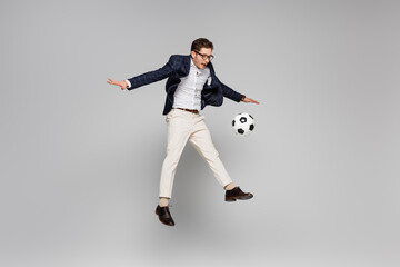 Fototapeta na wymiar full length of cheerful businessman playing football while levitating on grey