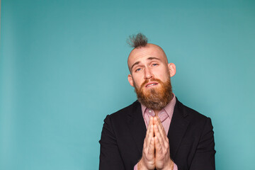 Bearded european businessman in dark suit isolated on turquoise background begging and praying with...
