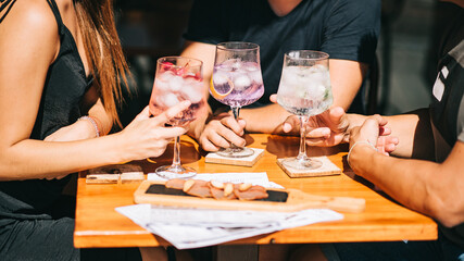Group of friends sitting on the summer terrace holding cocktails and snacks on the table. without faces