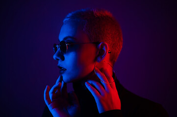 Portrait of a beautiful young woman with short hair in sunglasses in neon light