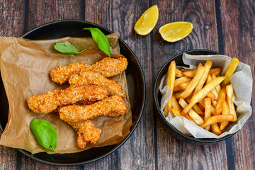 
 Crispy  deep fried   chicken strips  with sesame seeds and french fries . Breaded  with cornflakes chicken  breast fillets  with chilly peppers and fresh   basil on wooden rustic background