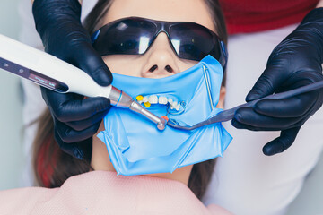 Close up of a female dentist examines the teeth of a young woman with a dental instrument in a...