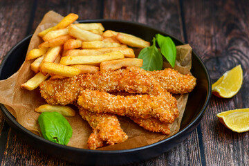 
 Crispy  deep fried   chicken strips  with sesame seeds and french fries . Breaded  with cornflakes chicken  breast fillets  with chilly peppers and fresh   basil on wooden rustic background
