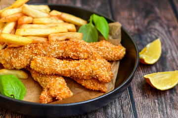 
 Crispy  deep fried   chicken strips  with sesame seeds and french fries . Breaded  with cornflakes chicken  breast fillets  with chilly peppers and fresh   basil on wooden rustic background