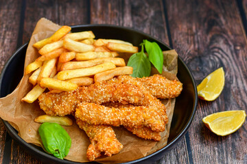 
 Crispy  deep fried   chicken strips  with sesame seeds and french fries . Breaded  with cornflakes chicken  breast fillets  with chilly peppers and fresh   basil on wooden rustic background