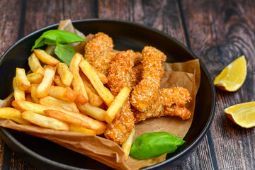 
 Crispy  deep fried   chicken strips  with sesame seeds and french fries . Breaded  with cornflakes chicken  breast fillets  with chilly peppers and fresh   basil on wooden rustic background