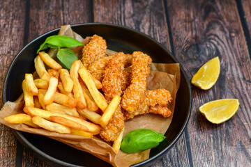 
 Crispy  deep fried   chicken strips  with sesame seeds and french fries . Breaded  with cornflakes chicken  breast fillets  with chilly peppers and fresh   basil on wooden rustic background