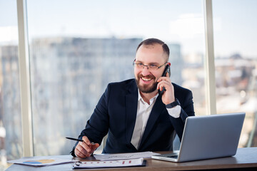 Adult male businessman, teacher, mentor looks at a laptop in his office. Office work. Development of a new business project