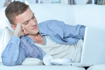 Fototapeta premium handsome young man lying on white couch with laptop