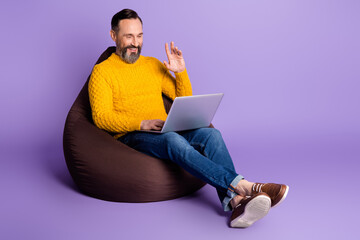 Full size profile photo of handsome guy sitting arm wave look laptop screen isolated on violet color background