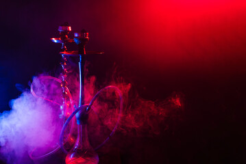 Modern hookah, shisha on a smoky black background with colored lighting and smoke. Close-up and place for your text