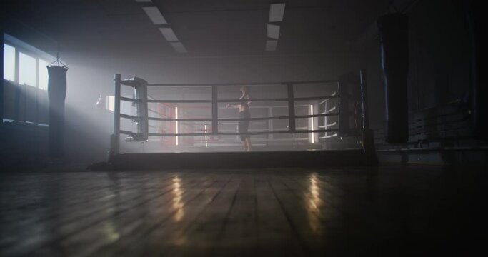 Young Woman Boxer With her Hands Wrapped in Bandage Jumping on Rope in Dark Ring Space a Gym with Smoke.