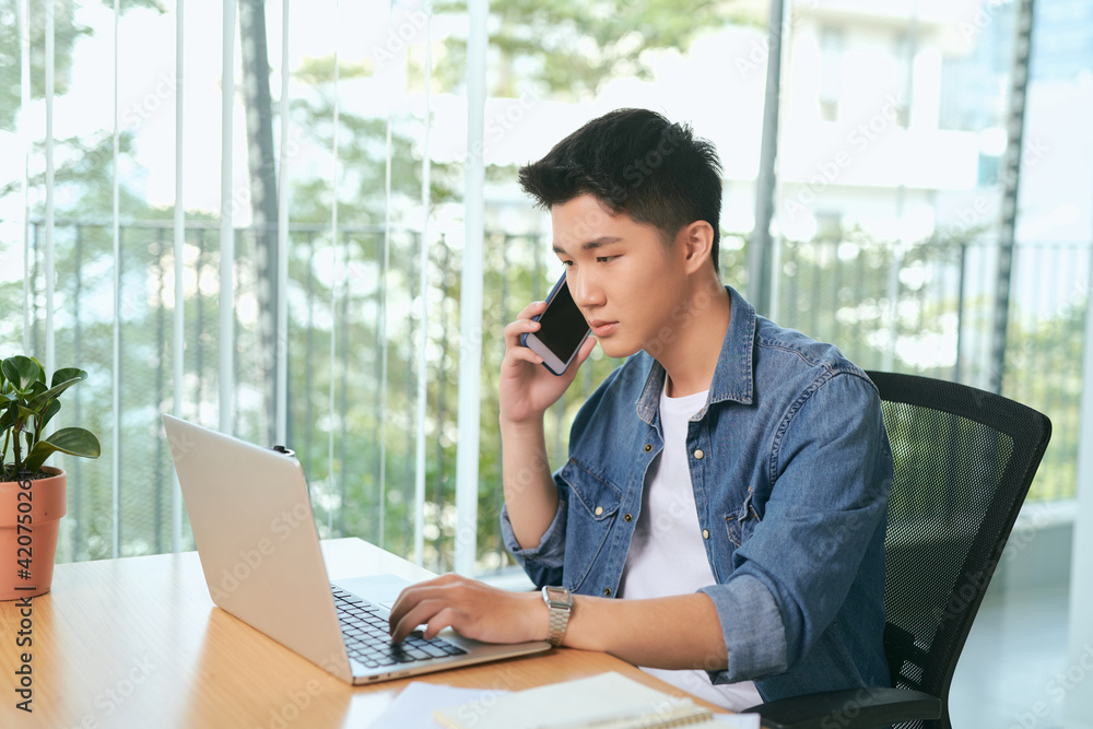 Poster smiling man writing notes while making phone call and using laptop at home