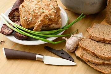 baked meat, soup and blood sausage on a plate, green onion and garlic on wooden background, home...