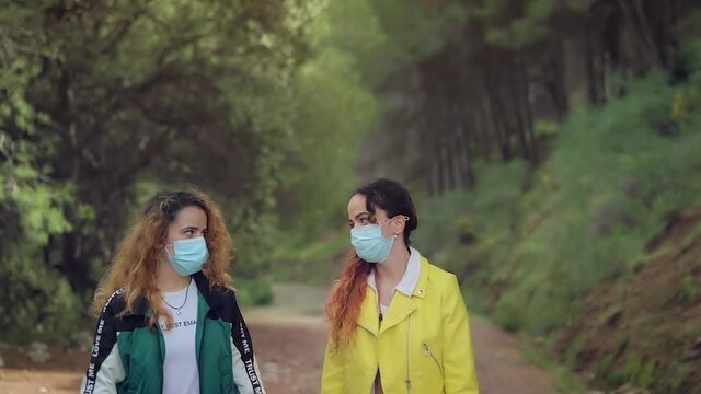 Hermanas gemelas con mascarillas contra el virus charlando en el bosque