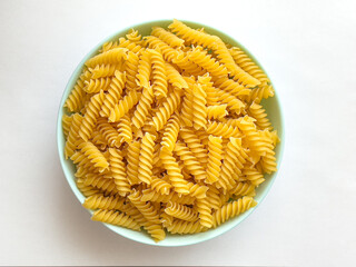 Raw dry Italian pasta in shape of spiral in bowl on wooden table at kitchen. Food background. Top view. Uncooked macaroni.