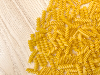Food background or texture raw dry Italian pasta in shape of spiral on wooden table or desk. Closeup, macro, top view. Uncooked macaroni.